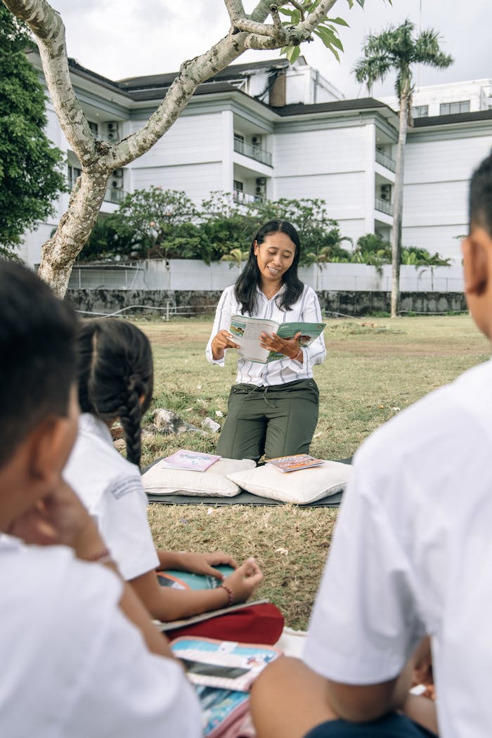 Teacher reading to children outdoors in a sunny setting, promoting education