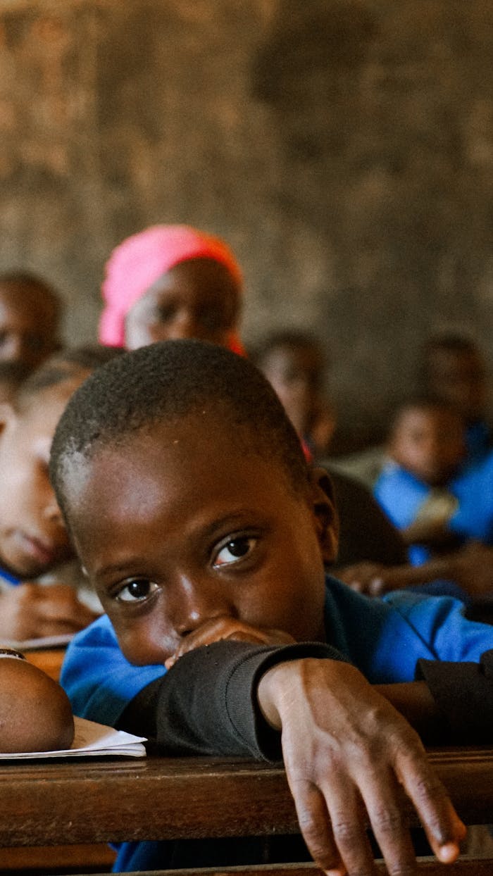 A child in a classroom looks thoughtfully, surrounded by peers in a learning environment.